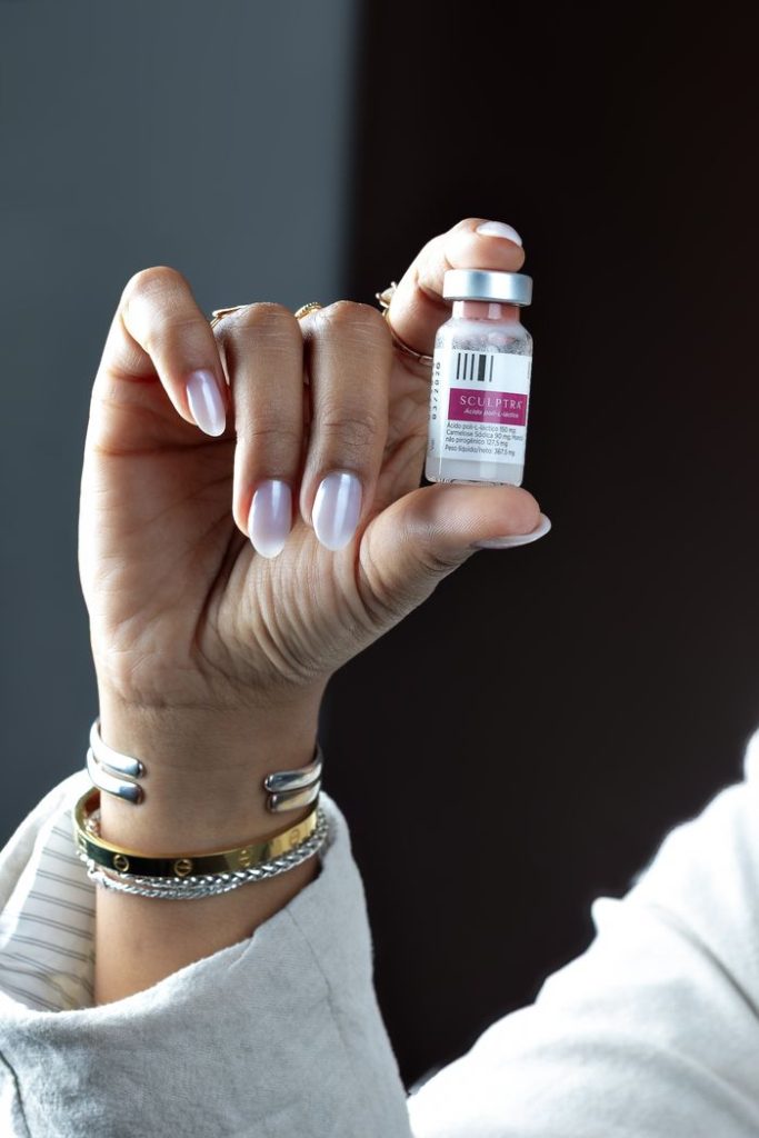 Detail of a persons hand holding a Sculptra cosmetic vial against a dark background.