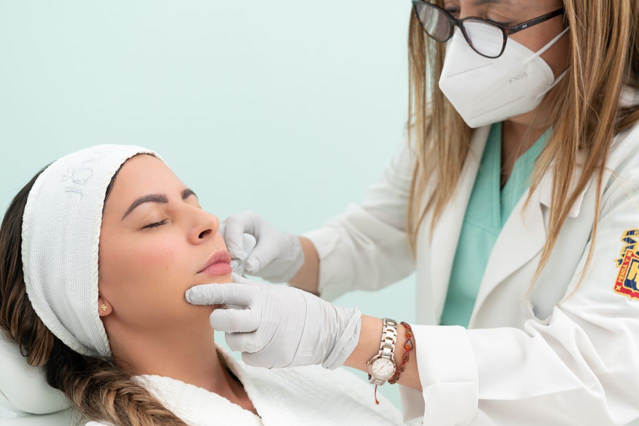 Doctor performing cosmetic treatment on a woman with eyes closed in a clinical setting.
