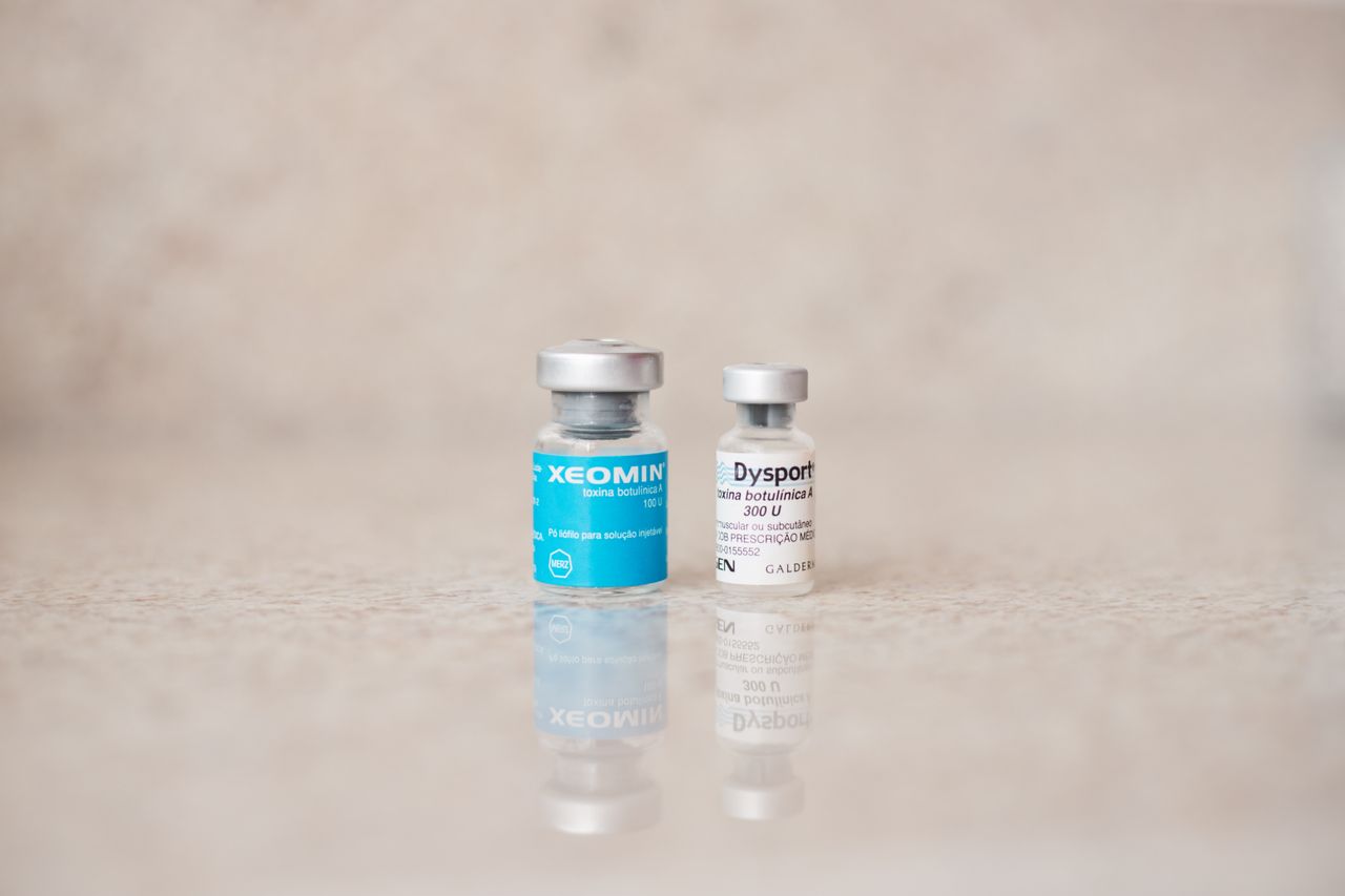 Close-up of Xeomin and Dysport bottles reflecting on a surface, shot indoors.
